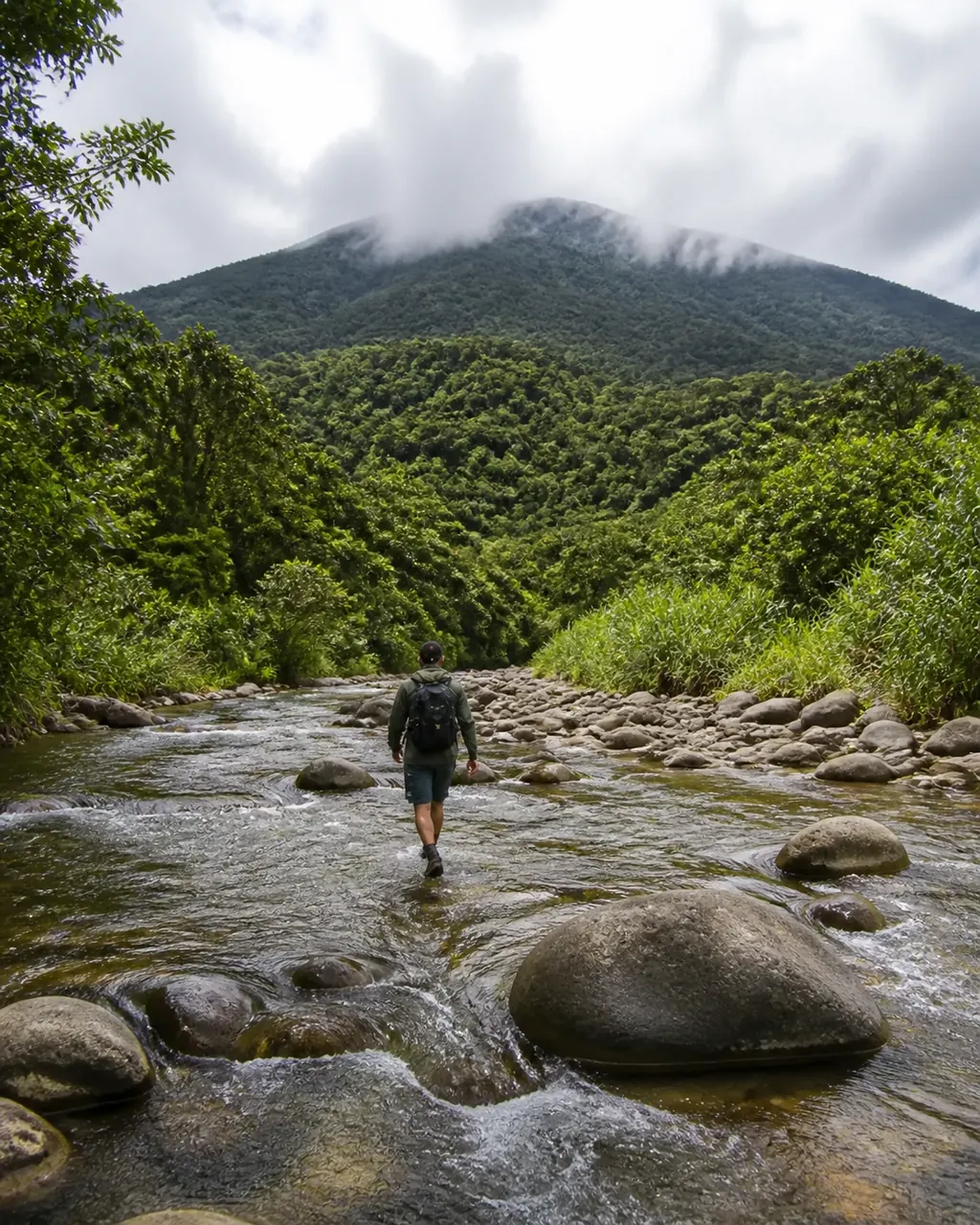 Hiker crossing a rainforest river beneath a Costa Rican volcano